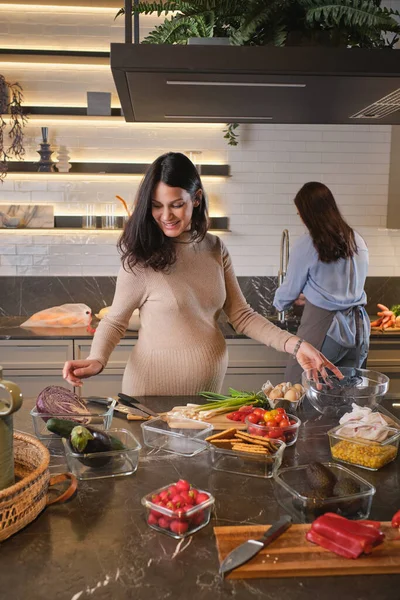 Smiling women in casual clothes having fun while cooking healthy lunch in kitchen at home