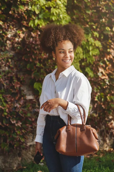 Lächelnde Afroamerikanische Unternehmerin Schickem Freizeitoutfit Mit Handtasche Steht Grünen Busch — Stockfoto