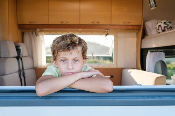 stock image Relaxed boy with crossed arms looking at camera while resting behind window of modern caravan during summer vacation