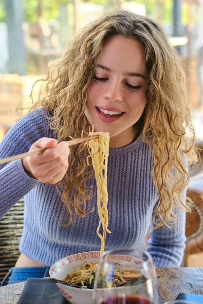 上周末 身穿蓝色毛衣 笑着在餐馆里用筷子吃辣面条的积极女性 — 图库照片