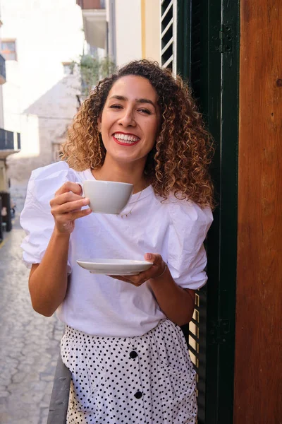 上周末 穿着休闲装的年轻女性站在城市街道上方的阳台上喝茶 — 图库照片