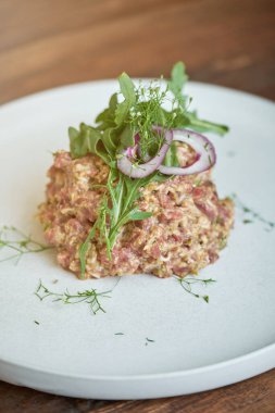 İştah açıcı biftek tartartarından soğan ve otlar ahşap masada beyaz tabakta servis edilir.