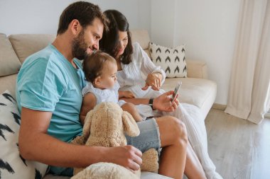 Kanepede oturup, akıllı telefondan video izlerken, evde birlikte vakit geçirirken aile manzarası.