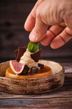 Krem şantili çikolata ve incir dilimli peynirli keki süsleme sürecinde tanınmayan şefin eli bulanık arka planda seramik tabakta servis ediliyor.