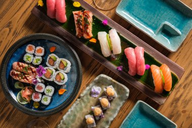Çeşitli suşi rulolarının ve pirinçli çiğ balığın ahşap masada servis edildiği Nigiri 'nin üst görüntüsü.