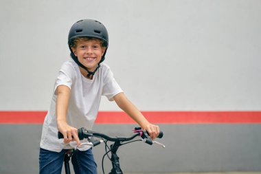 Koruyucu kasklı pozitif çocuk bisiklete biniyor ve kameraya bakarken gülümsüyor.