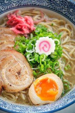 Yukardan taze pişmiş ramen çorbası, yumurta ve narutomaki ile seramik kasede servis edilir.