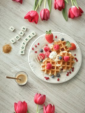 Masada böğürtlenli tatlı waffle 'ların üzerinde I Love Gofres yazıları ve açık mutfakta kahve var.