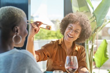 Gülümseyen kıvırcık saçlı, sandalyeye oturmuş, toplantı sırasında lezzetli suşi yiyen etnik bir kadın.
