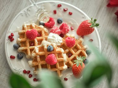 Taze böğürtlenlerle servis edilen tatlı waffleların ve bulanık yeşil bitkilerle açık mutfakta sunulan ballı dipbalığın yukarısından.