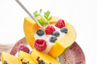 Yoğurtlu lezzetli meyveli papaya tatlısı ve beyaz arka planda servis edilen kaşıklı böğürtlen.