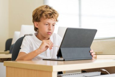 Okulun modern sınıfında okurken Stylus 'u tablette kullanan zeki bir öğrenci.