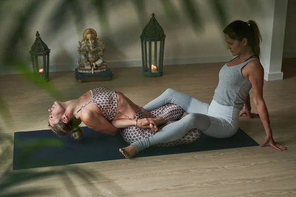 Full body of flexible female athletes in activewear sitting on mat and doing stretching exercise while practicing yoga in modern studio