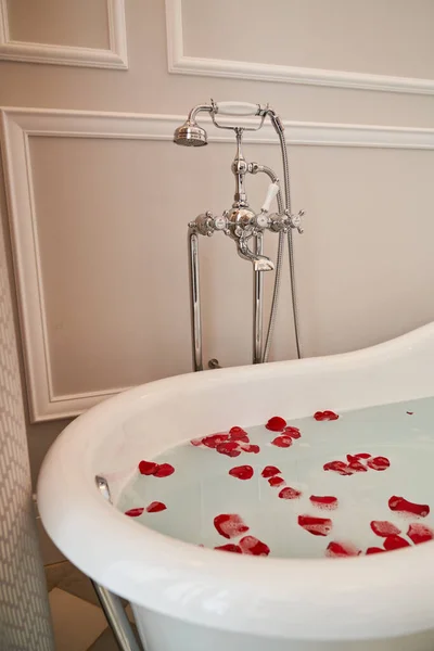 ホテルのスイートにあるバラの花びらとヴィンテージの蛇口で覆われた水が付いている浴槽の内部 — ストック写真