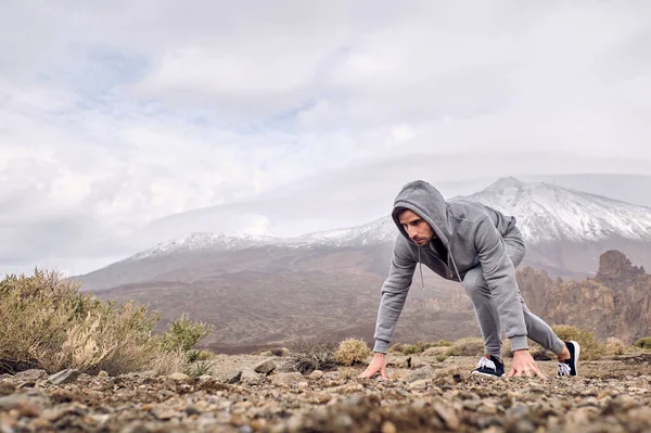 サイドビューのフルボディの焦点を当てたヒスパニック系男性旅行者スポーツウェアで立っクルックスタート位置で山に対して石の地面にTeideでテネリフェ島カナリア諸島スペイン — ストック写真