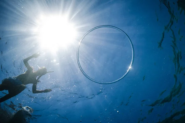 下からの眺めシュノーケリングマスクの無名の子供の水から明るい太陽の光の下でリングバブルと青い海に飛び込む — ストック写真
