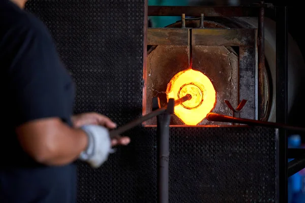 生産プロセス中に工場で炉にガラスオブジェクトを添付した鉄棒を置く匿名の男性労働者をクロップ — ストック写真