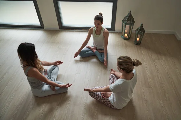 在瑜伽课上 穿着活动服坐在地板上静坐在莲花中冥想的年轻女性在工作室里的姿势 — 图库照片