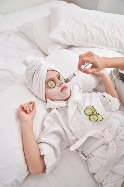 Crop Anonymous Mother Applying Moisturizing Mask Brush Face Kid Bathrobe — Stock Photo, Image