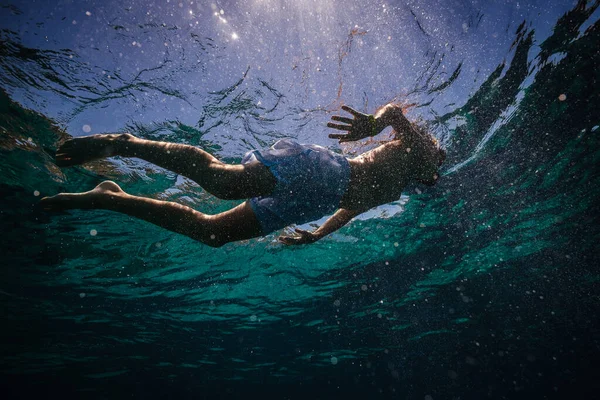 夏休みの間 青い海の中で水中でシュノーケリングを持つダイビングマスクの少年の下から — ストック写真