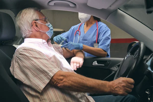 Anonimowy Lekarz Masce Oddechowej Strzykawką Zaszczepiającą Starszego Pacjenta Samochodzie Podczas — Zdjęcie stockowe