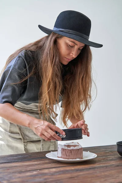 身穿休闲装头戴帽子 留着长长的波浪般的长发的年轻女性 正在准备美味的巧克力蛋糕 — 图库照片