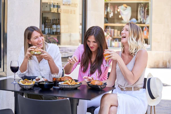 年轻女人 头发蓬松 坐在咖啡台旁边 一边吃着美味的汉堡包 一边吃着薯条和各种酒 一边玩 — 图库照片