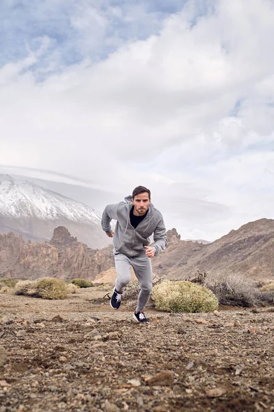 スポーツウェアを着た髭の男とスニーカーの全身スペインのカナリア諸島のティード火山の近くの石の地面に走る — ストック写真