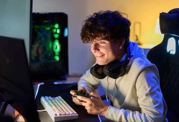 ゲームPcでテーブルに座り 部屋でジョイスティックでビデオゲームを一人でプレイしながら コンピュータの画面を見ながら笑顔の若い男性に焦点を当てた — ストック写真