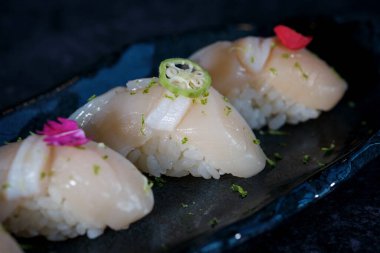 Lezzetli nigiri sushi, taze baharatlı çiçek, yeşil okro ve çiğ balıklı kırmızı biber, siyah masada mermer tabakta servis ediliyor.