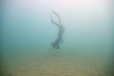 Dalgıç kıyafetli anonim sualtı balıkçısının ve zıpkınla derin deniz suyuna dalan yüzgeçlerinin tüm vücut görüntüsü.