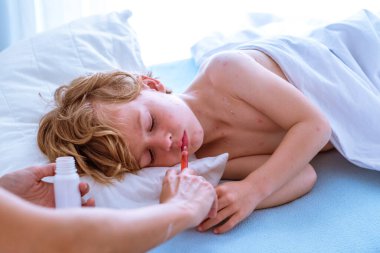 Yüksek açılı ekin annesi, evde güneşli yatak odasında uyuyan suçiçeği hastası uyuyan çocuğa şuruplu şırınga veriyor.