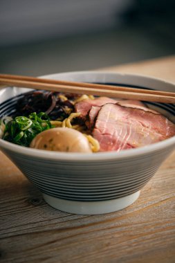 Bir kase lezzetli Japon ramen çorbası domuz eti parçaları ve yemek çubuklarıyla restorandaki ahşap masaya konmuş.