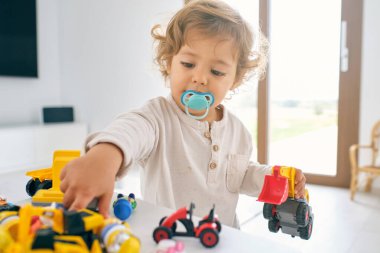 Güneşli bir günde bulanık arka planda renkli plastik oyuncaklarla oynayan sevimli küçük bir çocuk.