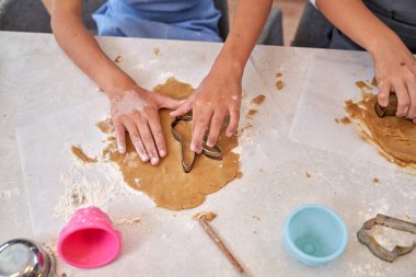 Yukarıdan gelen, önlüklü isimsiz çocuklar şık bir masada oturur ve mutfakta kurabiye hazırlarken metal şekillerle hamur keserler.
