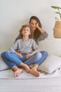 Huzurlu çocuk kıvırcık saçlı ve gözleri kapalı. Evde aydınlık bir odada otururken üstsüz annesini nazikçe kucaklıyor. 