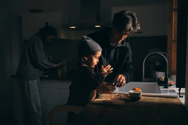 Mandalina soyan tatlı oğluna yardım eden genç adamın yan görüntüsü. Mutfakta, karısının yanında duruyor. Lezzetli bir akşam yemeği hazırlıyor.