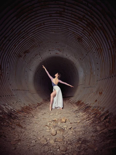 身材苗条的芭蕾舞女舞者在用石头跳舞的旧隧道中看着高举的胳膊的全景 — 图库照片