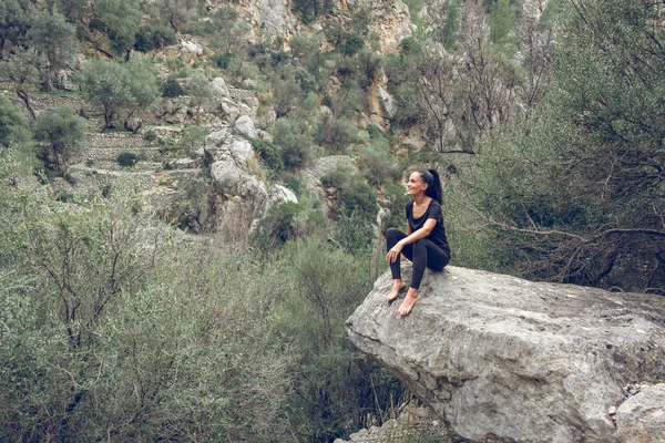 西班牙马略卡谷的一块巨石上坐着快乐的赤脚女人 身穿黑色衣服 笑着观察山脉 — 图库照片