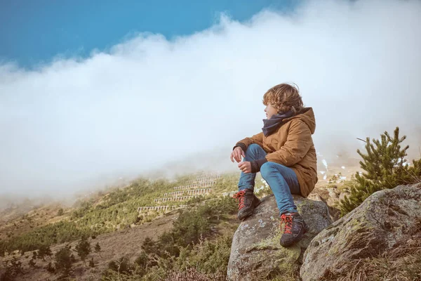 フルボディサイドカーリーヘアボーイ 暖かいアウターウェアに座って 蒸気雲で覆われた丘を賞賛 — ストック写真