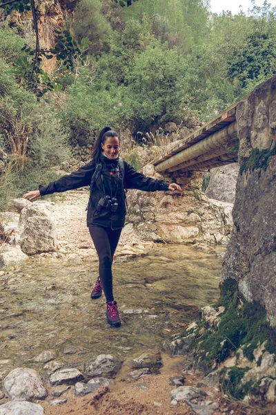 在索勒的旅程中 全身上下都是兴奋的西班牙裔年轻女旅行者 身穿暖和的休闲装 头戴马尾辫 在绿树成荫的山间穿行 面带微笑 — 图库照片