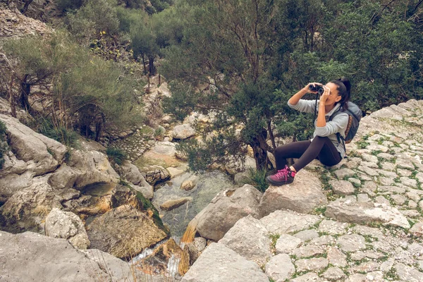在参观马略卡岛Soller地区Biniaraix村的过程中 从上方俯瞰着岩石悬崖边背包 用双筒望远镜欣赏风景如画的女性游客 — 图库照片