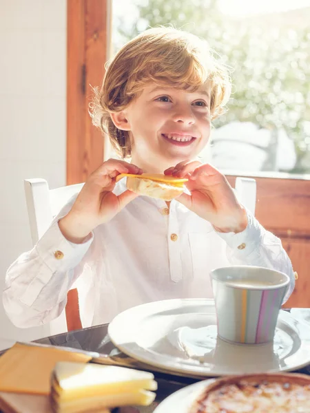 Uroczy Chłopiec Koszuli Jedzący Pyszne Kanapki Siedząc Przy Stole Filiżanką — Zdjęcie stockowe