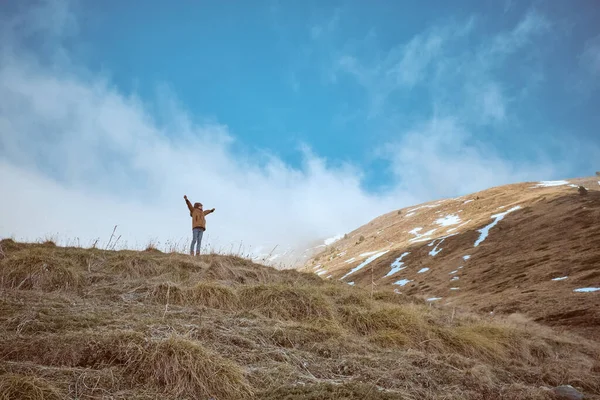 野生の丘の上に立っている外装の遠くの認識できない少年は 自然の中で寒い日に凍り付いた斜面の近くに腕を上げました — ストック写真