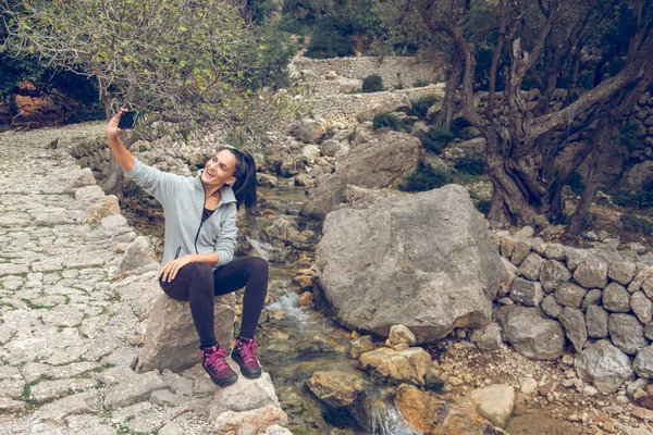 在Mallorca Soller Biniaraix 满身快乐的女人坐在溪流边的石头上 一边在手机上自拍 一边看着屏幕 — 图库照片