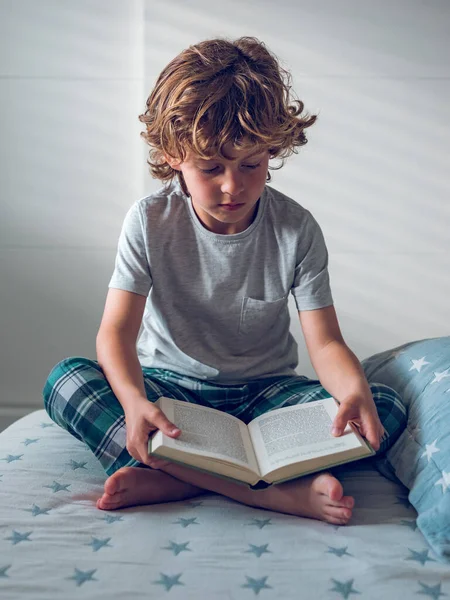 柔らかいベッドの上に足を横切って座って本でエキサイティングな物語を読んで焦点を当てた19歳の男の子のフルボディ — ストック写真