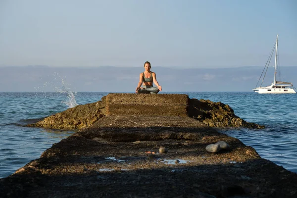 身穿运动服的无忧无虑的女运动员坐在石质码头上 手牵手在海滨的陀螺泥沼中摆姿势 — 图库照片