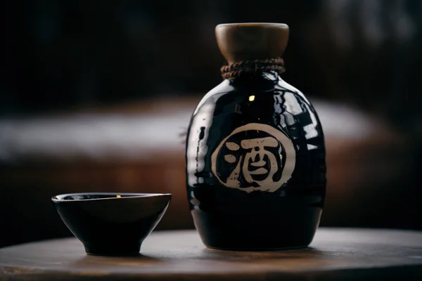 Japon sake şişesi ve ahşap masaya yerleştirilmiş küçük bardak restoranın bulanık arka planına karşı