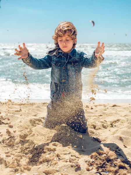 Bambino Che Indossa Giacca Jeans Seduto Sulla Spiaggia Gettando Sabbia — Foto Stock