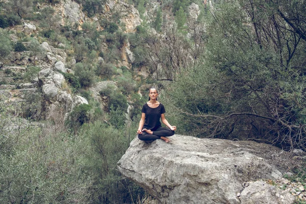 在石谷的巨石上坐着一长串身披黑发 身披紧闭双眼 双手握着瑜伽的和平的年轻女士 — 图库照片
